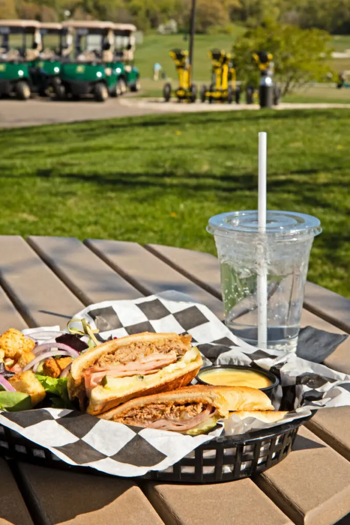 Cuban sandwich on table with glass of water, golf carts in background