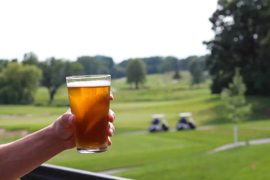Hand holding a pint of beer while overlooking golf course