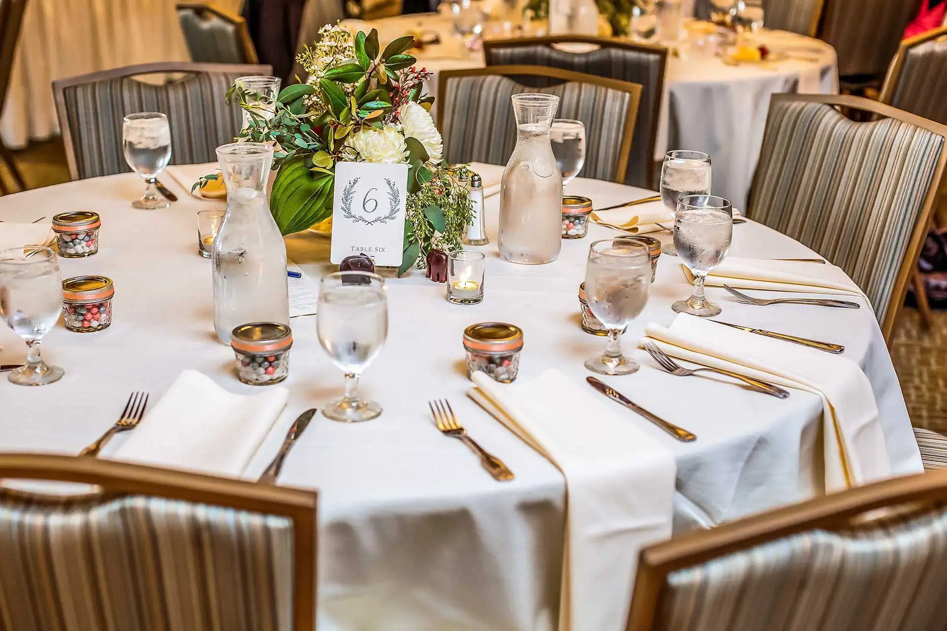 Table set for catered events with linens, silverware, floral arrangment and cups